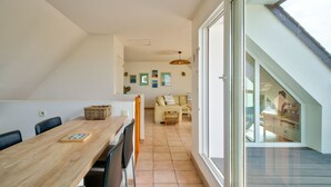 Un área de comedor con una mesa y sillas de madera, un sofá y una alfombra pequeña. Hay una ventana con vistas al exterior.