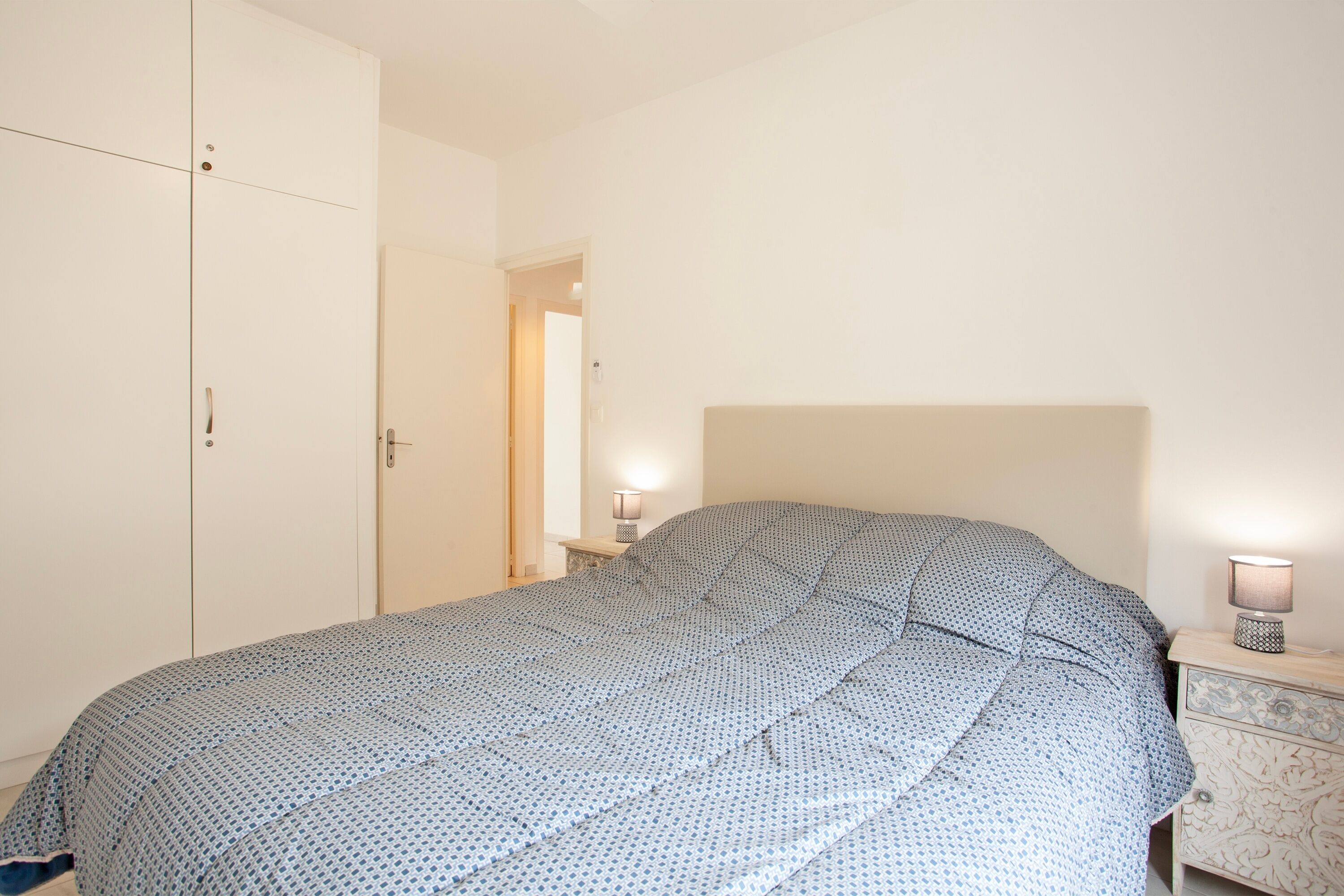 A bedroom with a bed, a wardrobe, a bedside table with a lamp, and a nightstand.