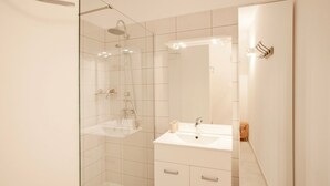 A modern bathroom with a glass shower enclosure, a white sink with a mirror above it, and a small wooden stool. - Alivi - Appt climatisé avec vue mer et montagne (L'Île-Rousse)