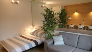 Een moderne slaapkamer met een bed, een grijze bank, een klein rond tafeltje en een grote spiegel.