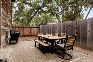 A backyard with a wooden deck, a barbecue grill, and a dining table with chairs.