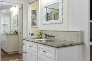 A bathroom with a white vanity, a granite countertop, and a mirror with an ornate frame.