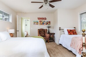 A bedroom with two beds, a ceiling fan, a chair, and artwork on the wall.