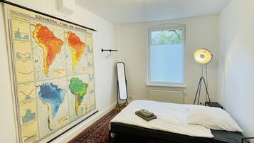 A bedroom with a bed, a map on the wall, a standing lamp, and a window.