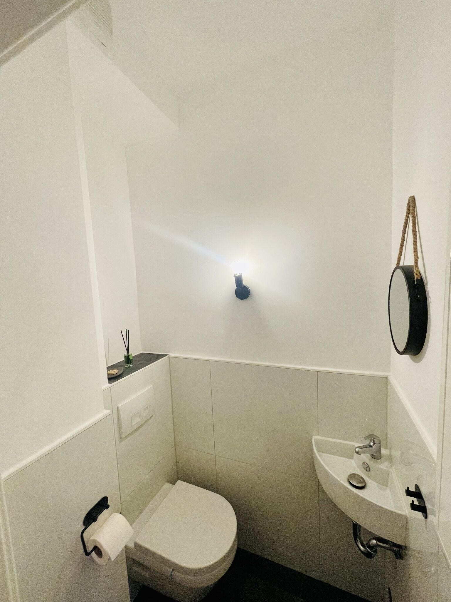 A small, white bathroom with a toilet, sink, and a wall-mounted mirror.