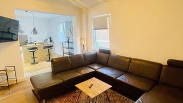 A modern living room with a sectional sofa, a patterned rug, and a dining area visible in the background.