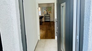 Un pasillo que lleva a una habitación con una puerta oscura, piso de baldosas y un cuadro en la pared.