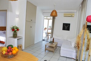 Een moderne, goed verlichte kamer met een bed, een eettafel met fruit, een kleine tafel met een plant en een hanglamp.