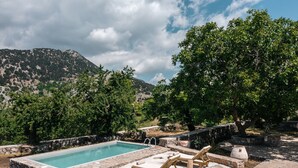 A pool area with stone walls and lounge chairs, surrounded by trees and a mountainous backdrop. - Nomas house Imbros,Private pool (Imbros)