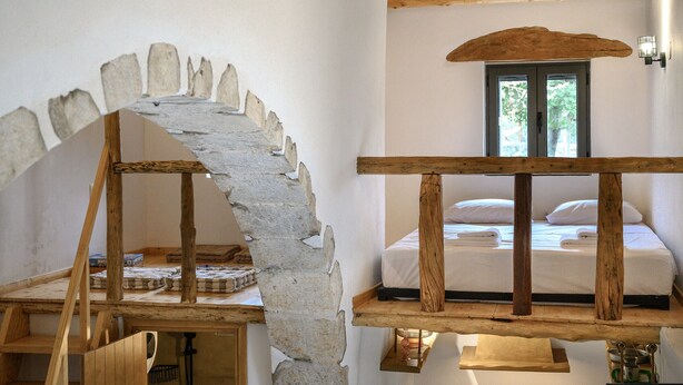 A rustic room with a stone archway, wooden beams, a bed with white linens, and a window with a view of trees. - Nomas house Imbros,Private pool (Imbros)