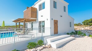 Et toetagers hvidt hus med pool, en træpergola og trapper op til indgangen.