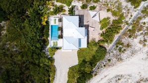 Oversigtsbillede af et moderne hus med swimmingpool, omgivet af frodig vegetation og et sandareal.