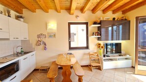 Una cocina con vigas de madera, un comedor con mesa y bancos, un televisor y una ventana con vistas.