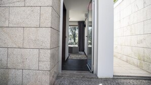 A narrow hallway with a stone wall on one side and a glass door on the other, leading to a room with a dark floor and a view of trees outside. - Casa da Magnólia (Briteiros (Santo Estêvão))