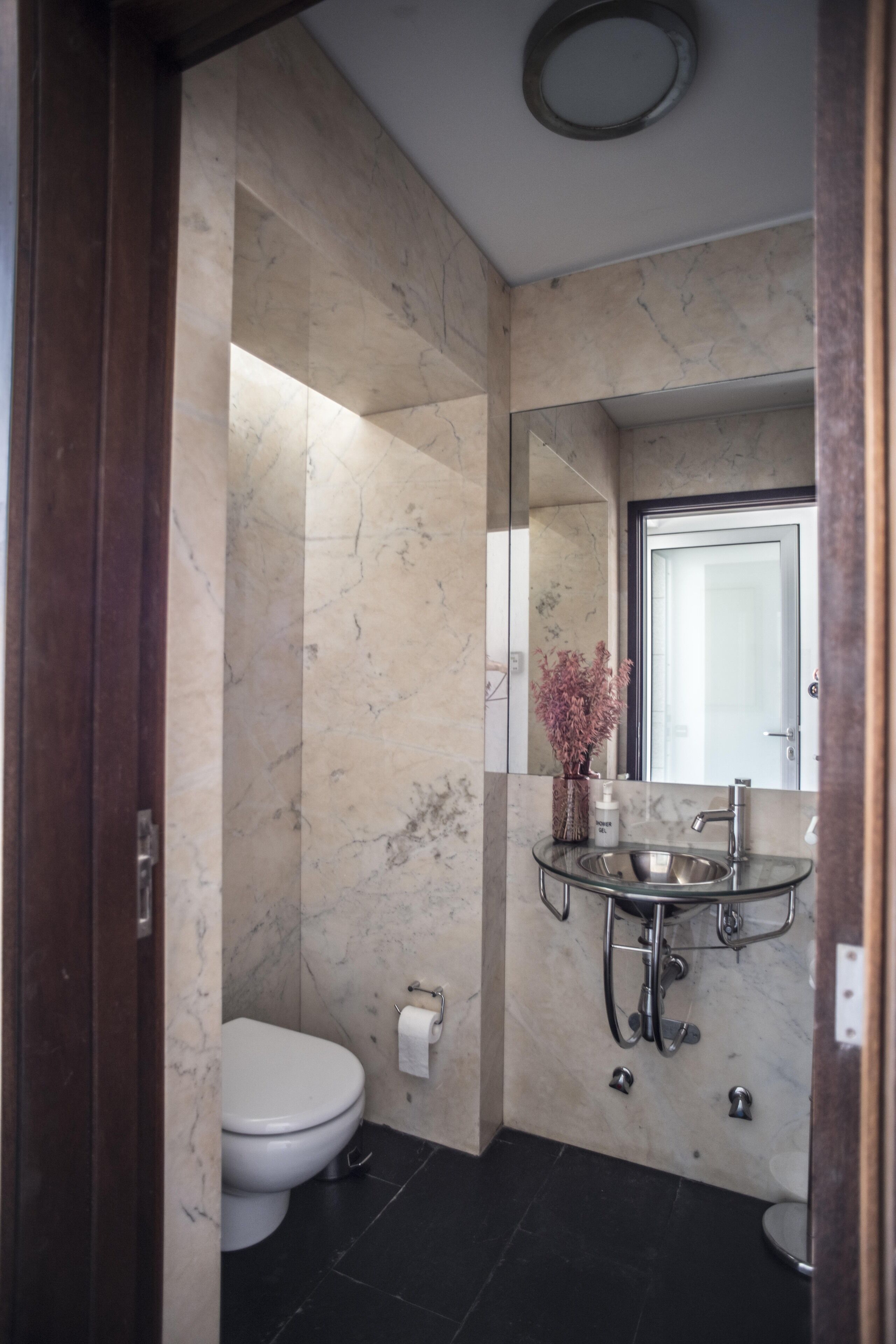Un baño con pared de mármol, lavamanos de cristal, inodoro y espejo.