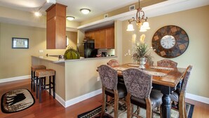 A dining area with a wooden table and chairs, a chandelier, and a decorative wall clock.