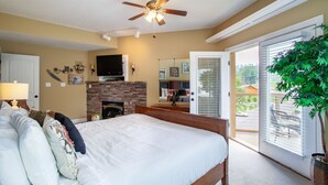 A bedroom with a large bed, a ceiling fan, a fireplace, and a sliding glass door to the outside.