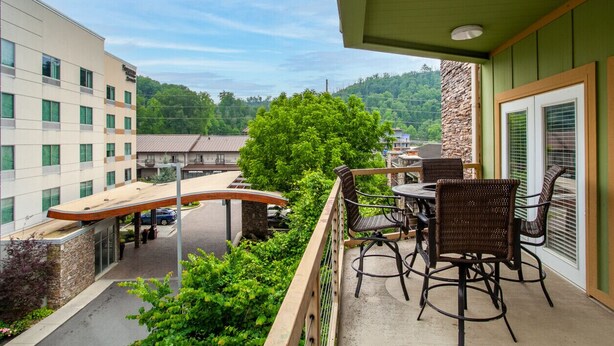 A balcony with wicker chairs and a table, overlooking a parking area and buildings.