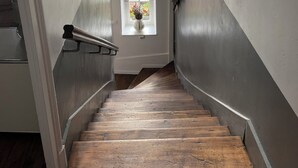 Een smalle trap met houten treden die uitkomt op een plateau met een klein raam.
