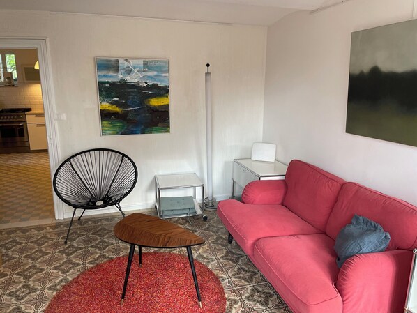 A living room with a red sofa, a black chair, a small wooden table, and a painting on the wall.