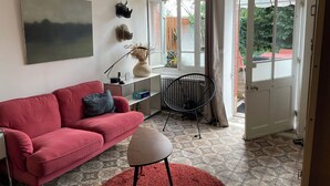 Een woonkamer met een rode bank, een klein rond tafeltje, een zwarte stoel en een groot raam met gordijnen.