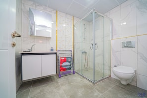 Une salle de bain moderne avec une douche à parois de verre, des toilettes blanches et un meuble-lavabo avec un miroir.