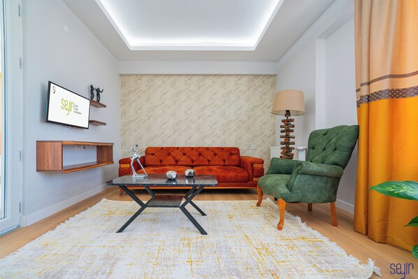 Un salon moderne avec un canapé, un fauteuil vert, une table basse, une lampe et un téléviseur fixé au mur.