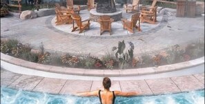 Ein Poolbereich mit einer Person, die im Wasser entspannt, umgeben von Gartenmöbeln und einer Feuerstelle.