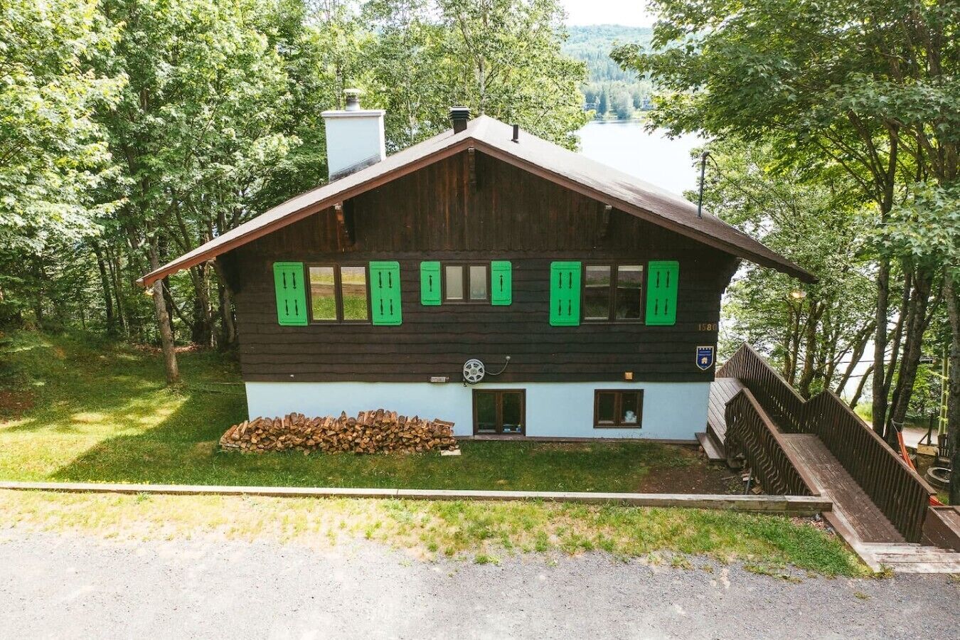 Una cabaña con techo inclinado, contraventanas verdes y una chimenea.