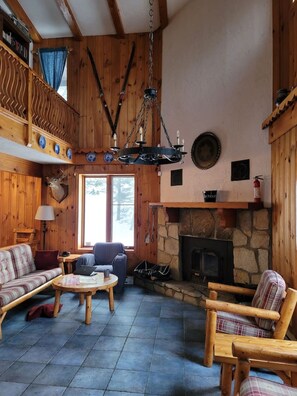 A cozy cabin interior with a stone fireplace, wooden furniture, and a hanging chandelier.