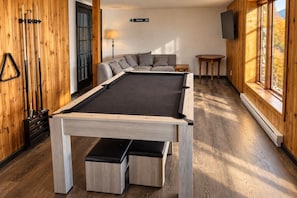 Una mesa de billar en una habitación con paredes de madera, un sofá y una lámpara.