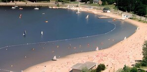 Una extensa masa de agua con varios veleros, una playa arenosa y algunos edificios al fondo.