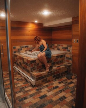 Una persona en un baño con piso de baldosas, una bañera y paredes de madera.