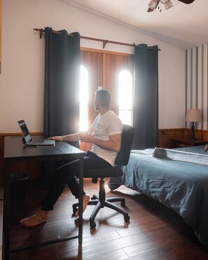 Una habitación con escritorio, silla, cama, lámpara y ventana con cortinas.