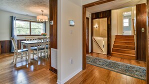 A spacious dining area with a wooden table and chairs, a window with curtains, and a staircase leading to another level. - Aiken Rd - 6 BR - hot tub and game room (Asheville)