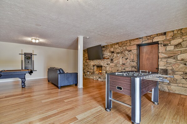 A room with a foosball table, a pool table, a stone wall, and a fireplace. - Aiken Rd - 6 BR - hot tub and game room (Asheville)