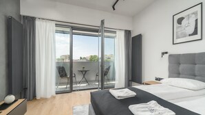 Een moderne slaapkamer met een groot bed, uitzicht door een schuifdeur op een terras en een kunstwerk in een lijst aan de muur.
