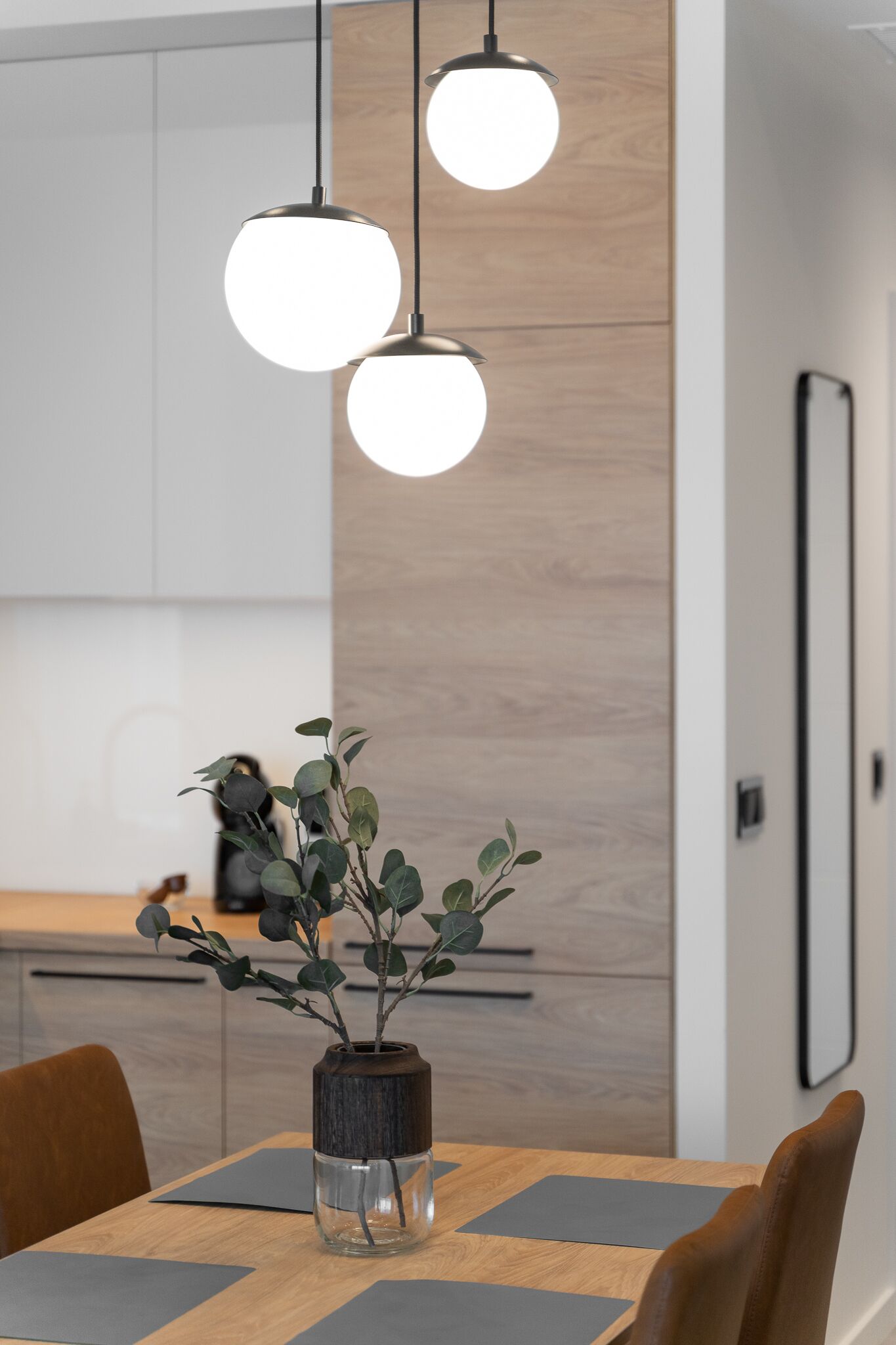 A modern kitchen with wooden cabinets, a dining table with chairs, and pendant lights.
