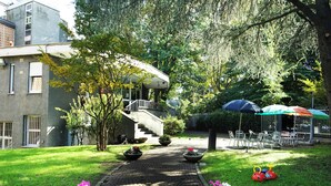 A courtyard with a paved walkway, outdoor seating, and a building with a staircase. - Hi! Ostello Milano (Milan)