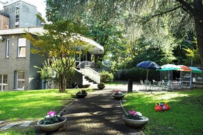 Un patio con un camino empedrado, plantas en macetas, mobiliario exterior y una escalera que conduce a un edificio.