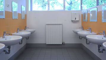 Baño público con cuatro lavamanos, espejos y un radiador.