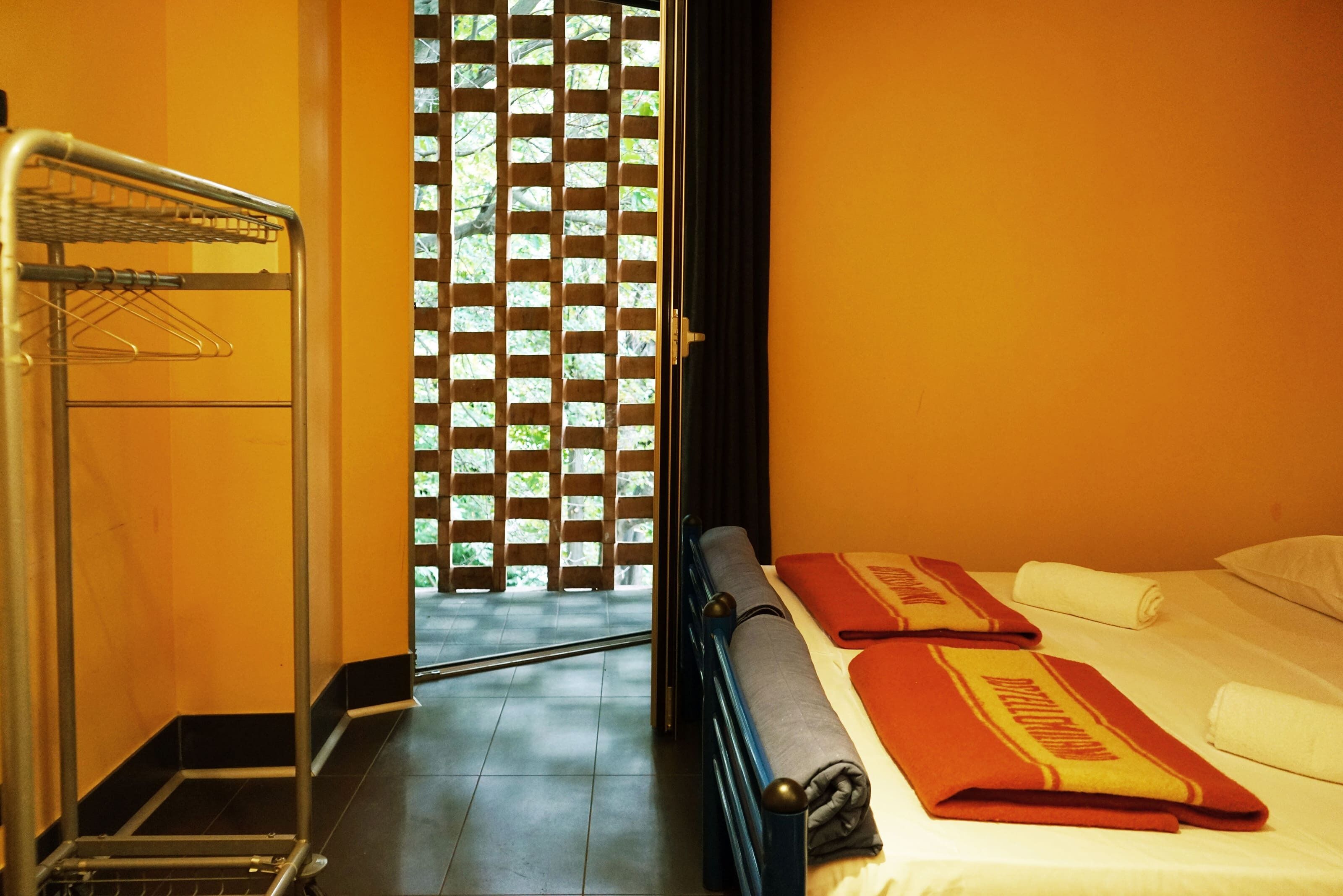 Camera d'albergo con un letto, un portasacchi e vista attraverso una finestra con un pannello decorativo.