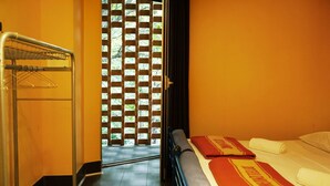 A hotel room with a bed, a towel rack, and a view through a window with a lattice screen. - Hi! Ostello Milano (Milan)