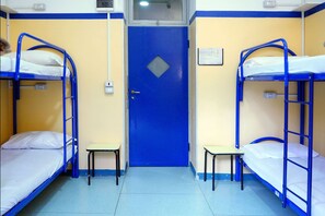 A dormitory room with two bunk beds, a small table, and a door with a window. - Hi! Ostello Milano (Milan)