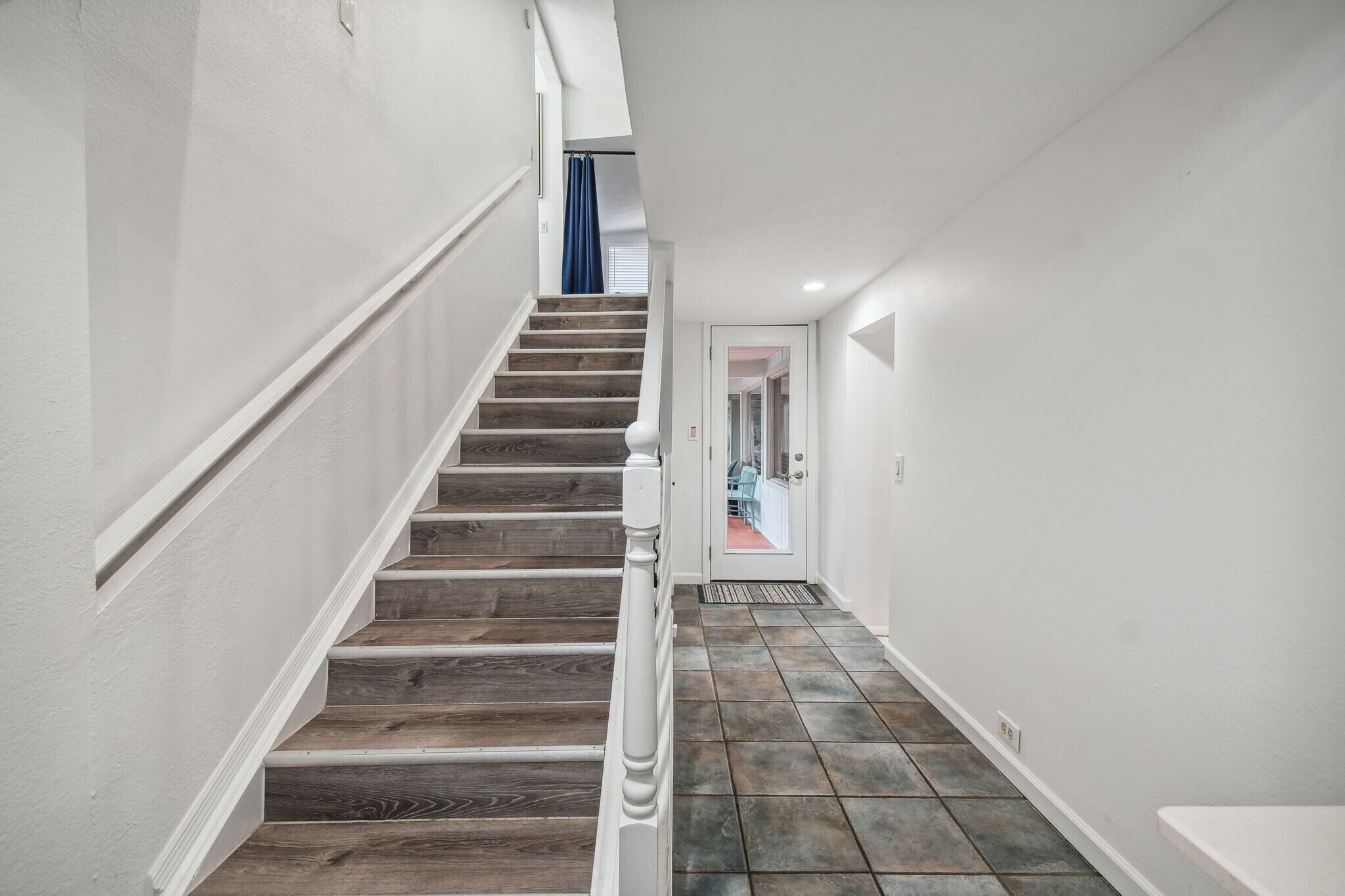 A staircase with wooden steps and white railings leading to a room with a tiled floor.