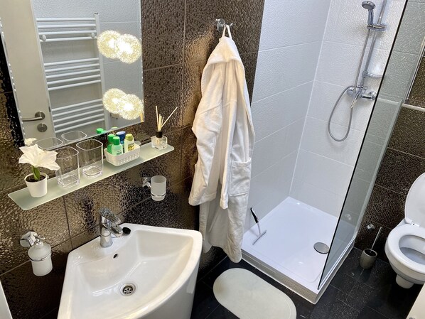 Une salle de bain moderne avec un lavabo blanc, une douche en verre, des toilettes et une serviette suspendue à un porte-serviettes.