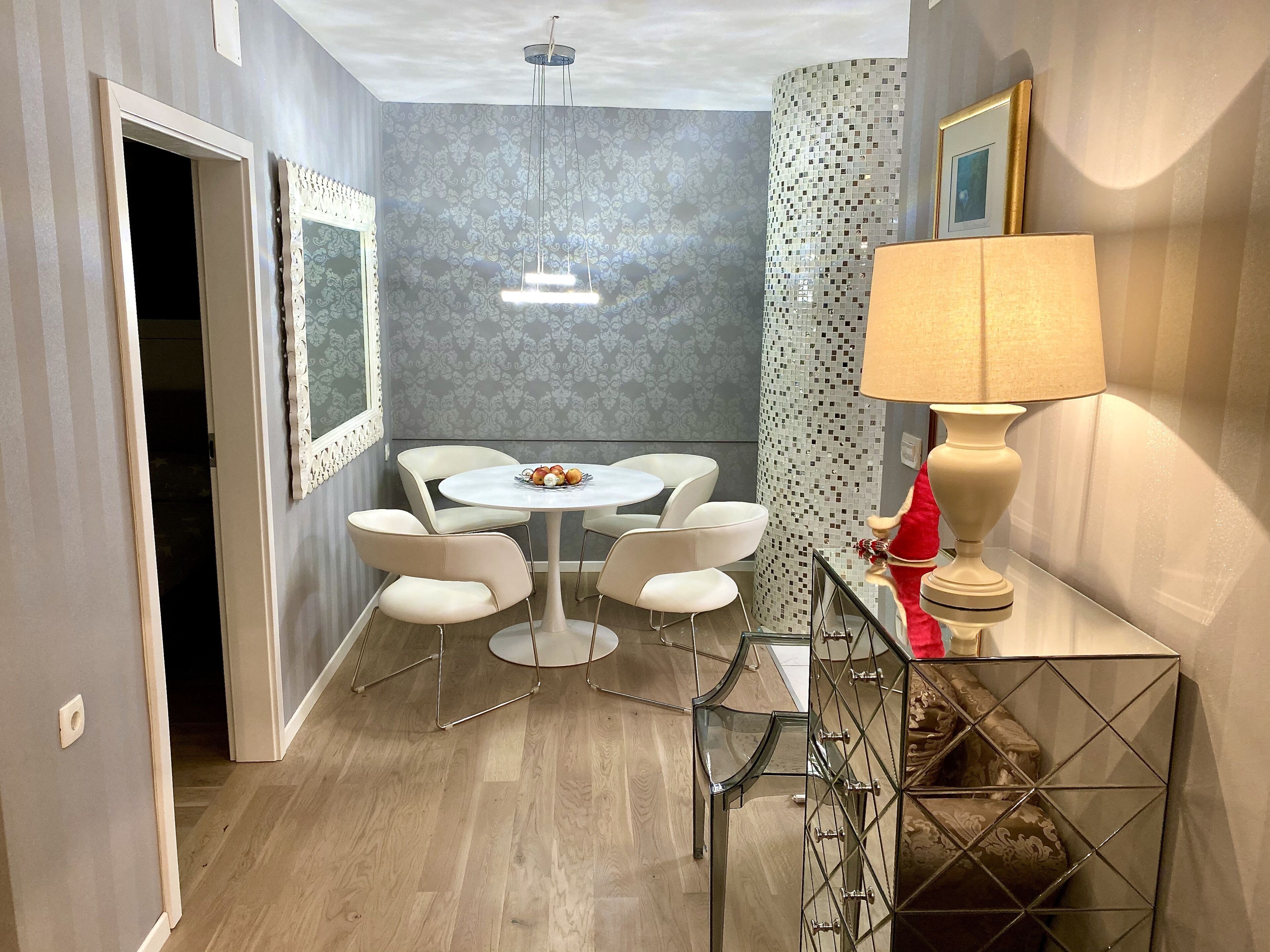 A modern dining area with a round table and white chairs, a decorative mirror, and a wall with a mosaic pattern.