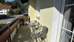 A balcony with two metal chairs and a small table, overlooking a street with parked cars and houses. - VYLD: Owl's nest (Bad Hindelang)