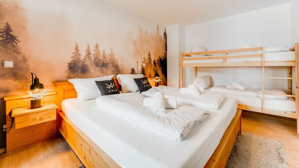 A bedroom with a large bed, a smaller bed, and a bunk bed. There is a nightstand with a lamp and a wall mural of trees. - VYLD: Owl's nest (Bad Hindelang)