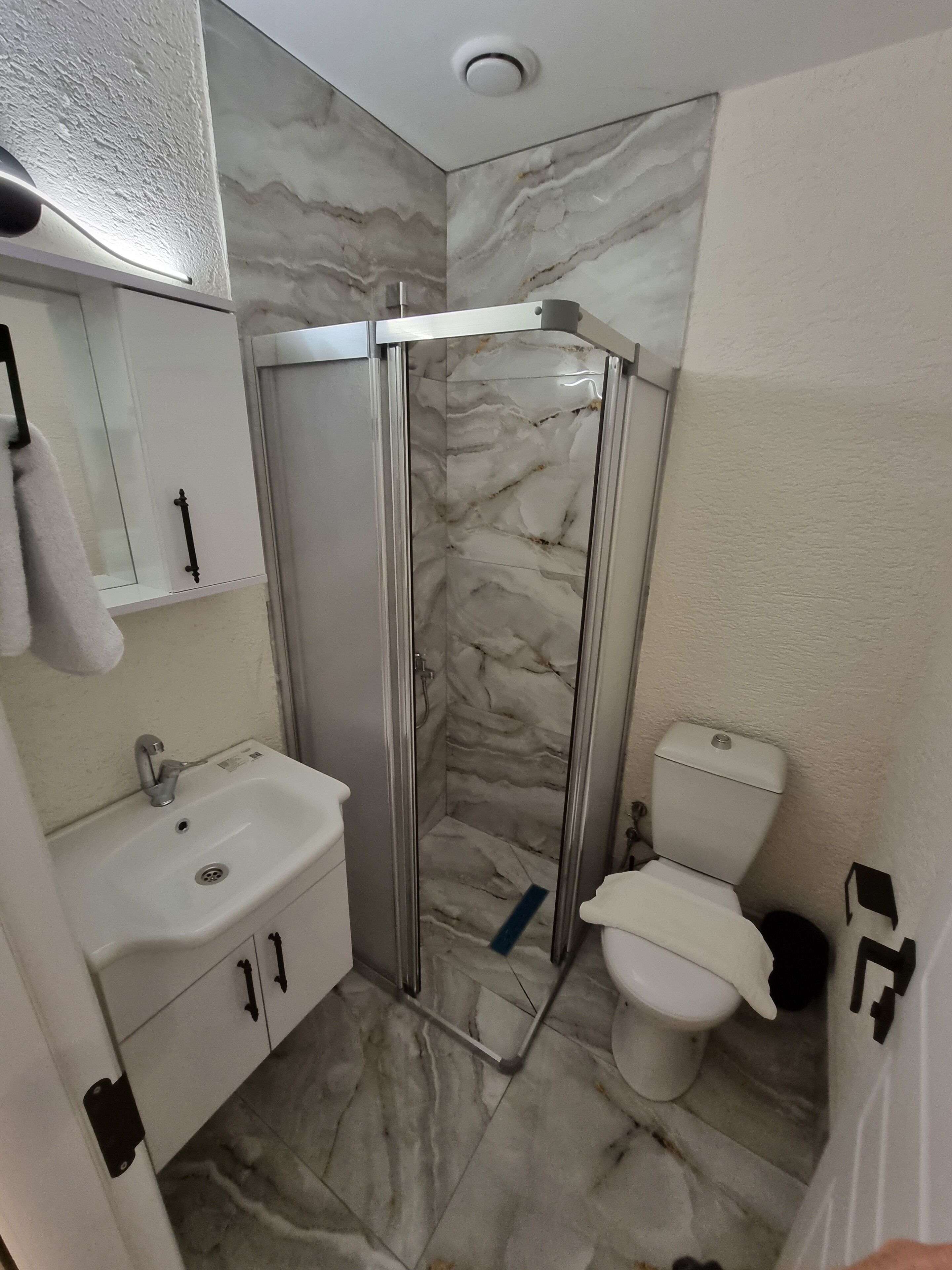 Un baño con lavamanos blanco, inodoro y cabina de ducha con paredes de mármol.